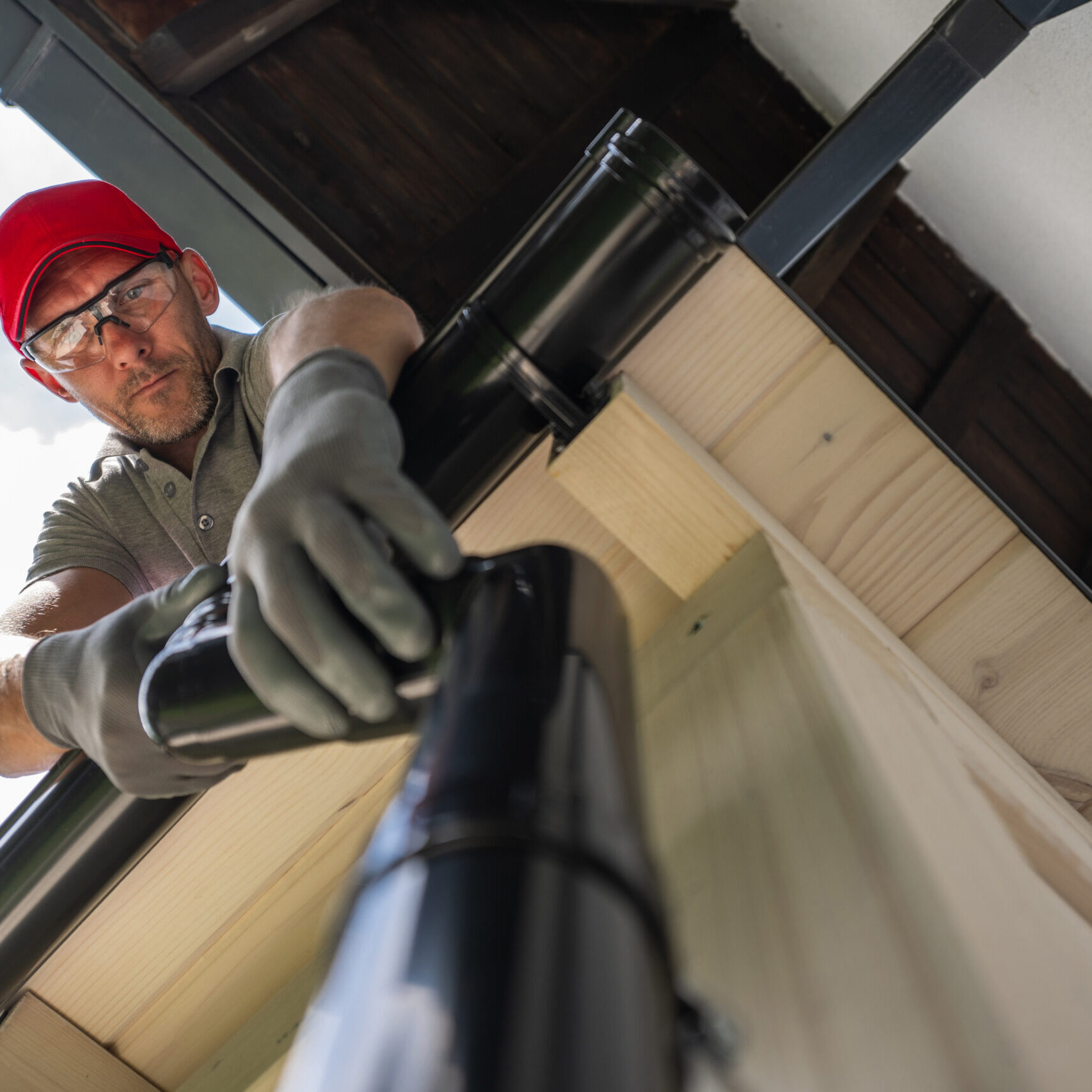 Man Cleaning Gutters On A Residential Roof On A Sunny Day Man Cleaning Gutters On A Residential Roof On A Sunny Day